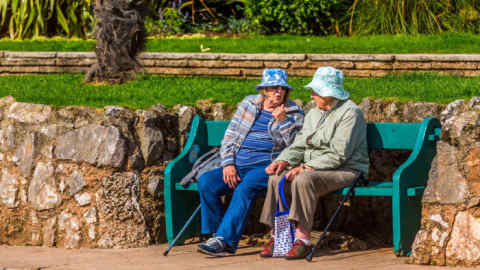 M0DDHH Two women friends chat together on a garden or park bench.