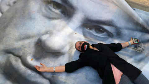 TOPSHOT - An Israeli woman wearing a face mask with &quot; crime minister&quot; written on it, lies on a banner during a &quot;Black Flag&quot; demonstration, to protest against Prime Minister Benjamin Netanyahu (image) and anti-democratic measures to contain the novel coronavirus outbreak, at Rabin Square in the coastal city of Tel Aviv, on April 19, 2020. (Photo by JACK GUEZ / AFP) (Photo by JACK GUEZ/AFP via Getty Images)