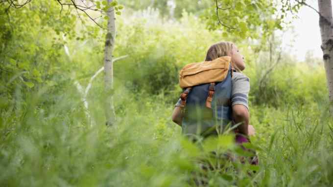 K4DPC4 Curious teenage girl with backpack hiking in tall grass in woods