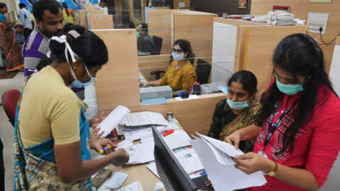 Bank clerks wearing a facemask amid concerns over the the spread of the COVID-19 coronavirus serve customers at a bank, in Bangalore on March 19, 2020. (Photo by Manjunath Kiran / AFP) (Photo by MANJUNATH KIRAN/AFP via Getty Images)