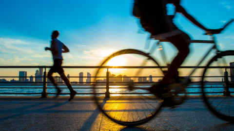 Silhouettes of jogger running and bicyclist cycling at sunset in front of the New York city skyline
Alamy