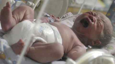 A newborn baby, one of 12 babies born by C-section, cries inside an incubator