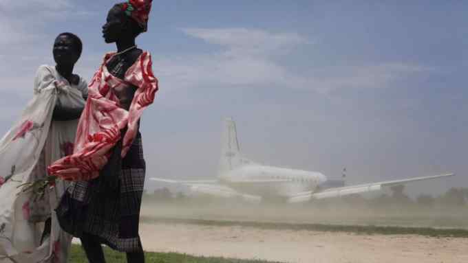 Women try to avoid dust as a plane, carrying nutrition supplements brought in by Medecins Sans Frontieres (MSF), lands in Leer July 15, 2014. The MSF hospital was giving service to over 200,000 people before it was looted and burned during fighting in late January and early February. The Hospital currently attends 1400 malnourished children according to Medecins Sans Frontieres. REUTERS/Andreea Campeanu (SOUTH SUDAN - Tags: HEALTH POLITICS SOCIETY FOOD TRANSPORT TPX IMAGES OF THE DAY) - RTR3YSC7
