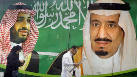 People walk past a banner showing Saudi King Salman, right, and his Crown Prince Mohammed bin Salman, outside a mall in Jiddah, Saudi Arabia, Saturday, March 7, 2020. (AP Photo/Amr Nabil)