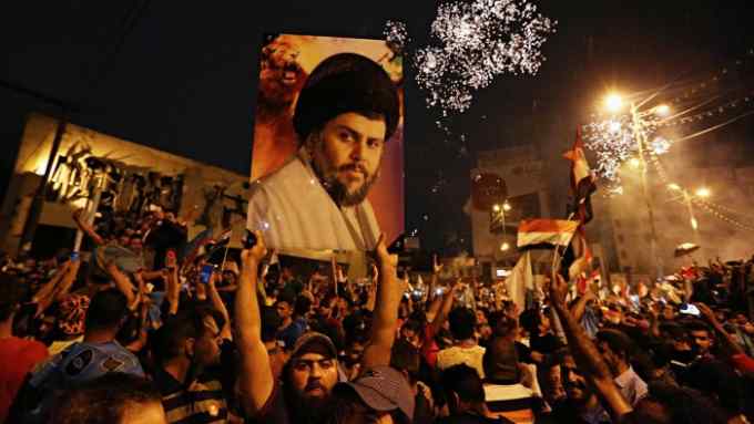 FILE - In this Monday, May 14, 2018 file photo, supporters of Shiite cleric Muqtada al-Sadr, carry his image as they celebrate in Tahrir Square, Baghdad, Iraq. Al-Sadr, who led punishing attacks on American forces after the 2003 U.S.-led overthrow of Saddam Hussein, appears set to secure the most significant victory of his political career with a strong showing in the May 12 parliamentary election. Al-Sadr gained popularity as a nationalist voice campaigning against corruption and against Iran‚Äôs influence in the country. (AP Photo/Hadi Mizban, File)