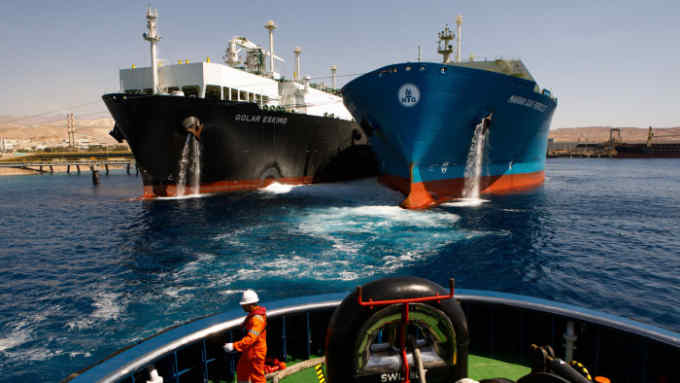 Bloomberg Best of the Year 2018: A crew member aboard the emergency standby ASD tug boat 'Tareq 3' watches as the 'Golar Eskimo' Floating Storage and Regasification Unit (FRSU), center right, takes on liquefied natural gas (LNG) from the 'Maran Gas Pericles' tanker at Aqaba port, operated by Aqaba Development Corp., in Aqaba, Jordan, on Wednesday, April 11, 2018. Photographer: Annie Sakkab/Bloomberg