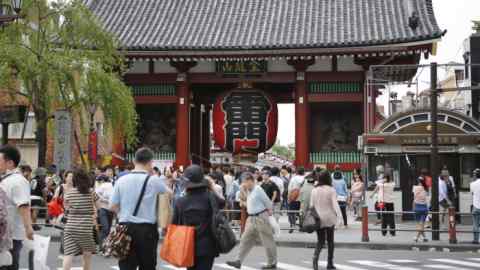 Visitors and tourists stand in front of the Kaminarimon, an entrance gate to the Sensoji temple, while others walk past in Tokyo, Japan, on Wednesday, May 6, 2015. Foreign visitors to the nation totaled 1.53 million people in March, the highest on record for a single month, according to a statement from the Japan National Tourism Organization. Photographer: Kiyoshi Ota/Bloomberg
