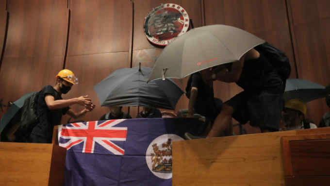 Protesters fix a British colonial flag to the parliament podium after they broke into the government headquarters in Hong Kong on July 1, 2019, on the 22nd anniversary of the city's handover from Britain to China. - Anti-government protesters stormed Hong Kong's parliament building late on July 1 after successfully smashing their way through reinforced glass windows and prizing open metal shutters that were blocking their way. (Photo by VIVEK PRAKASH / AFP)VIVEK PRAKASH/AFP/Getty Images