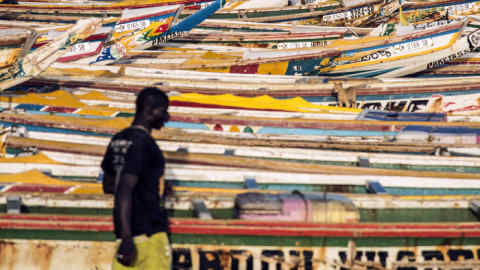 A man walks by hundreds of painted fishing boats at the Soumbedioune fish market in Dakar, Senegal, on Friday, July 28, 2017. Senegalese voters will elect a new parliament on Sunday in a vote that was marred by violence during campaigning as the ruling coalition is challenged by a 91-year-old former president and the imprisoned mayor of the capital, Dakar. Photographer: Xaume Olleros/Bloomberg