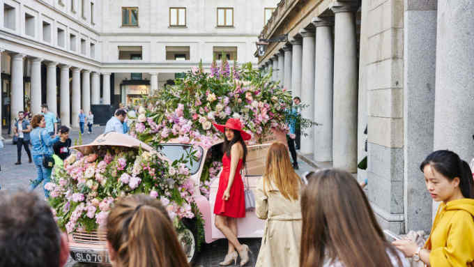 Tourists take photographs next to a Morris Minor stuffed with flowers as part of the Jo Malone floral display in the Covent Garden piazza. 19/05/2018
