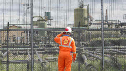 An employee speaks on a radio at the perimeter security fence of the Agbada oil flow station, operated by Shell Petroleum Development Co. (SPDC) in Port Harcourt, Nigeria, on Wednesday, Sept. 30, 2015.
