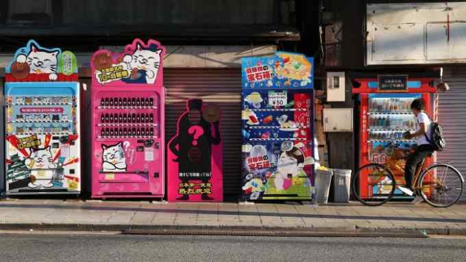 A man uses a 50-yen vending machine, right, while riding on a bicycle in Osaka, Japan, on Monday, Oct. 9, 2017. Amid the gloom and struggle that Osaka has gone through in recent years, a tourism boom has been an unexpected boon for Japan’s gritty second city. Photographer: Buddhika Weerasinghe/Bloomberg