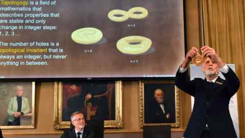 Thors Hans Hansson of the Nobel Committee for Physics uses a pretzel to visualise his explanation of topology, the branch of mathematics used by the winners