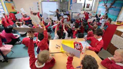 D1G5GG Primary junior school Mathematics Maths class, hands up with the answers, UK.