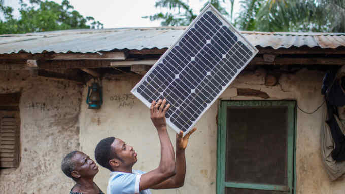 A young African farmer puts a solar panel on the roof of his house