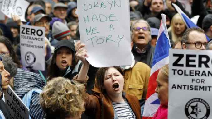 A woman holds up a placard declaring &quot;Corbyn made me a Tory&quot; as she joins protesters gathering for a demonstration organised by the Campaign Against Anti-Semitism outside the head office of the British opposition Labour Party in central London on April 8, 2018. Labour leader Jeremy Corbyn has been under increasing pressure to address multiple allegations of anti-Semitism within the party, which saw protesters gather outside the party's head office in London after Jewish campaigners demonstrated outside parliament two weeks ago. / AFP PHOTO / Tolga AKMEN (Photo credit should read TOLGA AKMEN/AFP/Getty Images)