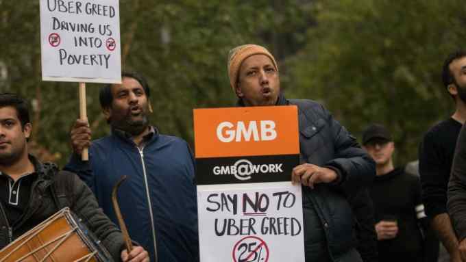 Uber drivers hold up signs during a protest against a rise in the commission taken by Uber Technologies Inc. outside their offices in London, U.K., on Thursday, Nov. 12, 2015. Uber Technologies Inc. got a boost from a London judge who said smartphones used by its drivers aren’t the same as taxi meters and don’t require a license from the city’s transport authority. Photographer: Simon Dawson/Bloomberg