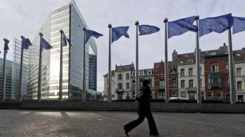 A pedestrian passes European Union (EU) flags outside the the European Commission headquarters, in Brussels, Belgium, on Monday, Dec. 19, 2011. European finance ministers will today seek to meet a self-imposed deadline for drawing additional aid to the debt crisis and to form new budget rules as investor confidence that a comprehensive solution is achievable wanes. Photographer: Jock Fistick/Bloomberg