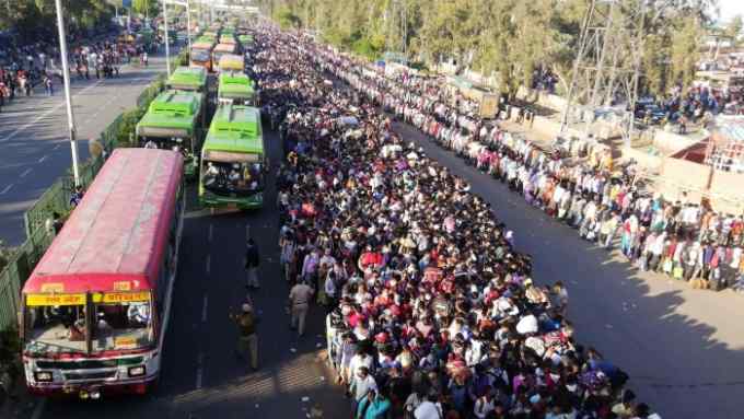 Migrant workers and their family members lineup outsdie the Anand Vihar bus terminal to leave for their villages during a government-imposed nationwide lockdown as a preventive measure against the COVID-19 coronavirus in New Delhi on March 28, 2020. - Tens of thousands of migrant workers and their famiies on March 28 fought and shoved their way onto buses organised by India's most populous state to get them to their home towns amid the coronavirus pandemic. (Photo by Bhuvan BAGGA / AFP) (Photo by BHUVAN BAGGA/AFP via Getty Images)