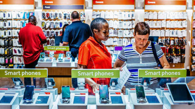 An employee assists a customer beside a display of smartphones at a mobile phone store inside the Vodacom World mall, operated by Vodacom Group Ltd., in the Midrand district of Johannesburg, South Africa, on Thursday, Feb. 2, 2017. Vodacom, which is 65 percent owned by Newbury, England-based Vodafone and the South African market leader by subscriber numbers, is expanding its internet offering to offset falling voice revenue. Photographer: Waldo Swiegers/Bloomberg