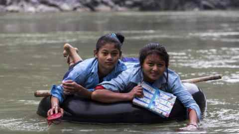 14-year-old Nepalese students use their sandals to paddle across the Trishuli river on a rubber ring to school each day in Dhading District