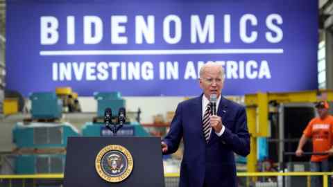 US President Joe Biden speaking from a stage with a backdrop sign saying ‘Bidenomics Investing in America’ behind him