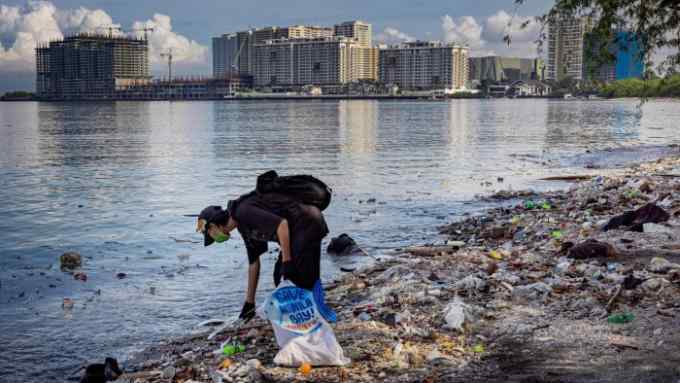 A volunteer collects plastic waste that washed up on the shores and mangroves of Freedom Island