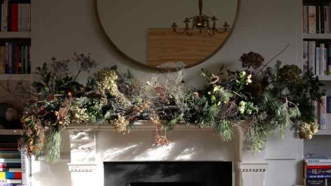 Green branches and dried flowers arranged on the mantelpiece, with sunlight streaming through the window