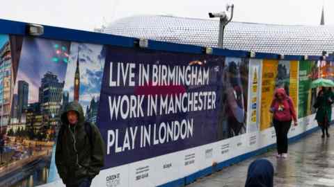 Hoardings on a street that read: Live In Birmingham, Work In Manchester, Play In London