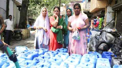 Four women wait as a man fills large cans with water