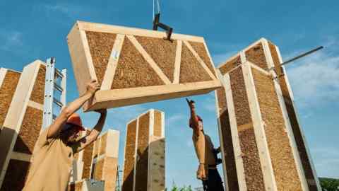 Builders manoeuvre a dangling panel of wood and straw made by Lithuanian company EcoCocon