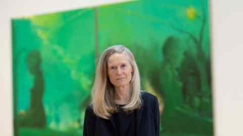 A blond woman in a black top poses in front of a green canvas