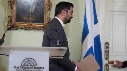 Hamza Yousaf walks away from a podium after speaking. A Scotland flag hangs in the background