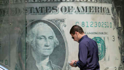 A man waits outside a currency exchange office displaying an image of the US dollar, in Cairo, Egypt