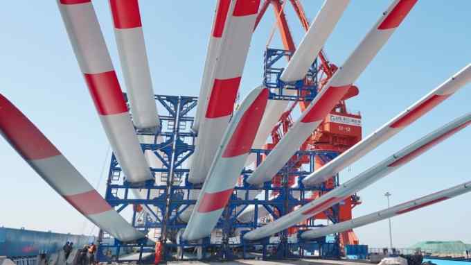 A crane loads red and white wind turbine blades on to a cargo ship in Yantai, China