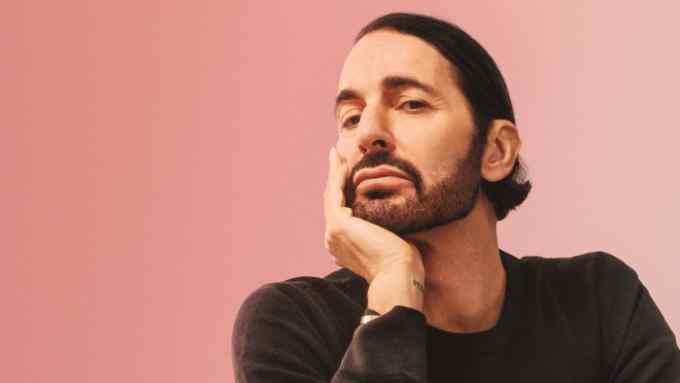Marc Jacobs sits on a yellow chair, chin resting in one hand