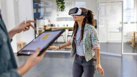 Young woman wearing virtual reality headset with another person holding a digital tablet