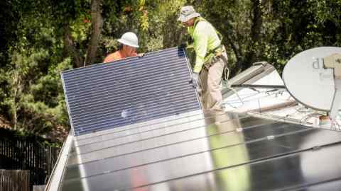 PetersenDean Inc. employees install solar panels on the roof of a home
