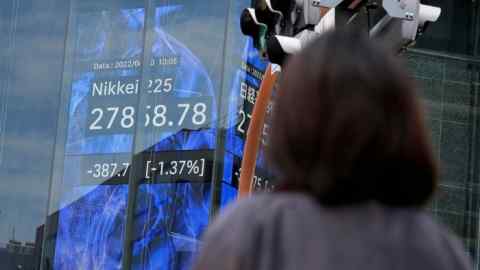 A woman stands in front of an electronic stock board in Tokyo