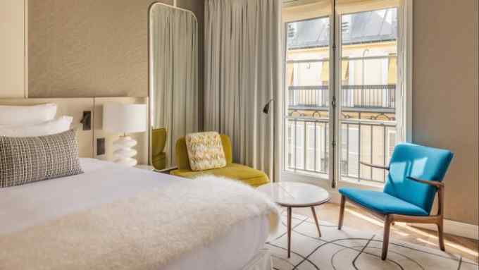 A beige-toned guest room at the Pavillon Faubourg Saint-Germain, with yellow and blue modernist wood chairs beside a French window