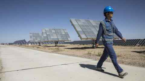 An employee walks past photovoltaic panels at a solar power station in China