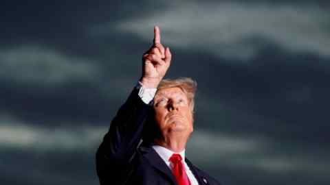 Donald Trump looks up while pointing to the sky against a stormy background