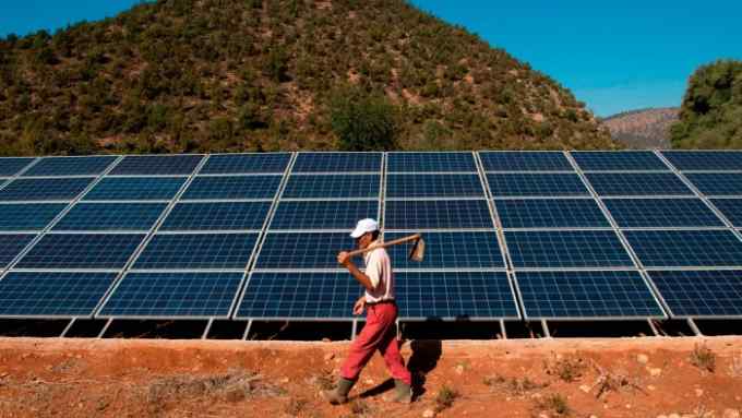 A Moroccan farmer walks past solar panels