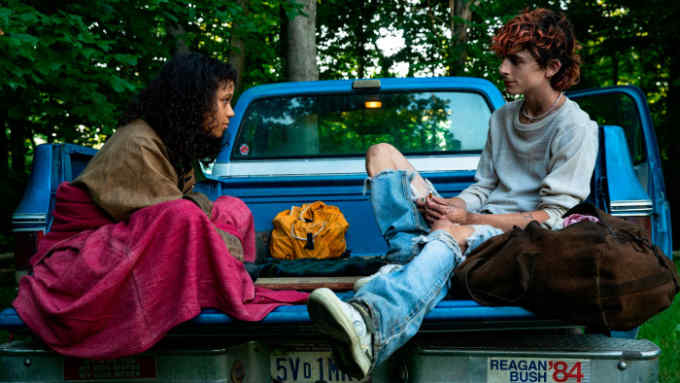 A young woman and a young man sit together on the open rear of a pick-up truck