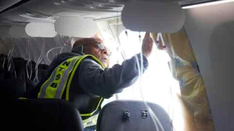An investigator examines the frame on a section of the Alaska Airlines aircraft