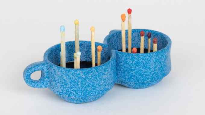 Small sculpture of two blue coffee cups with matches sticking up out of them