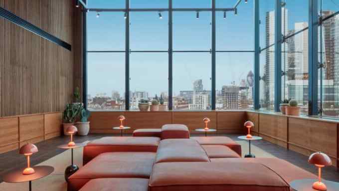 Pink-cushioned seating surrounded by a wooden wall and two floor-to-ceiling windows looking out over the City of London at One Hundred Shoreditch