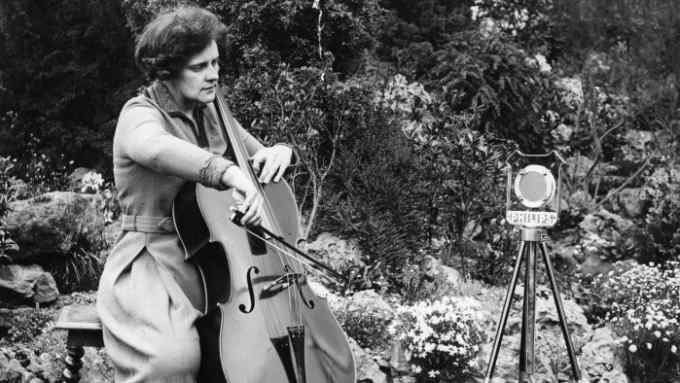 black and white photograph of woman playing a cello in a garden
