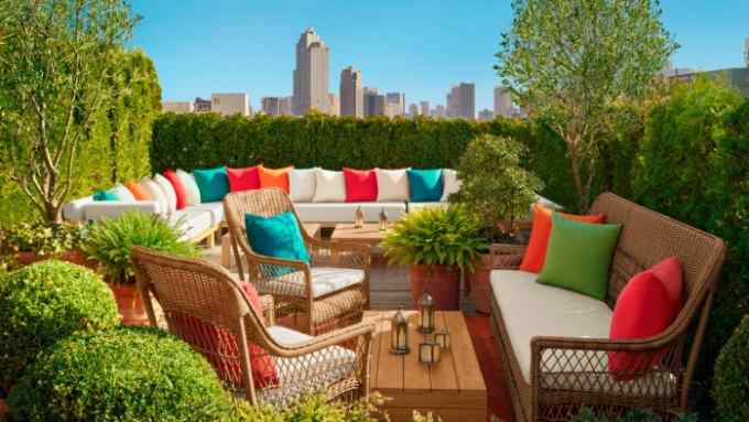 Brightly coloured cushions around a large white sofa in front of rattan chairs and a wooden table on the rooftop terrace at The Tokyo Edition, Ginza, which is dotted with shrubs and overlooks the city skyline