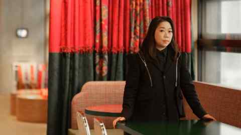 Gallerist Henrietta Tsui-Leung standing in front of a red curtain and by restaurant-style tables and chairs